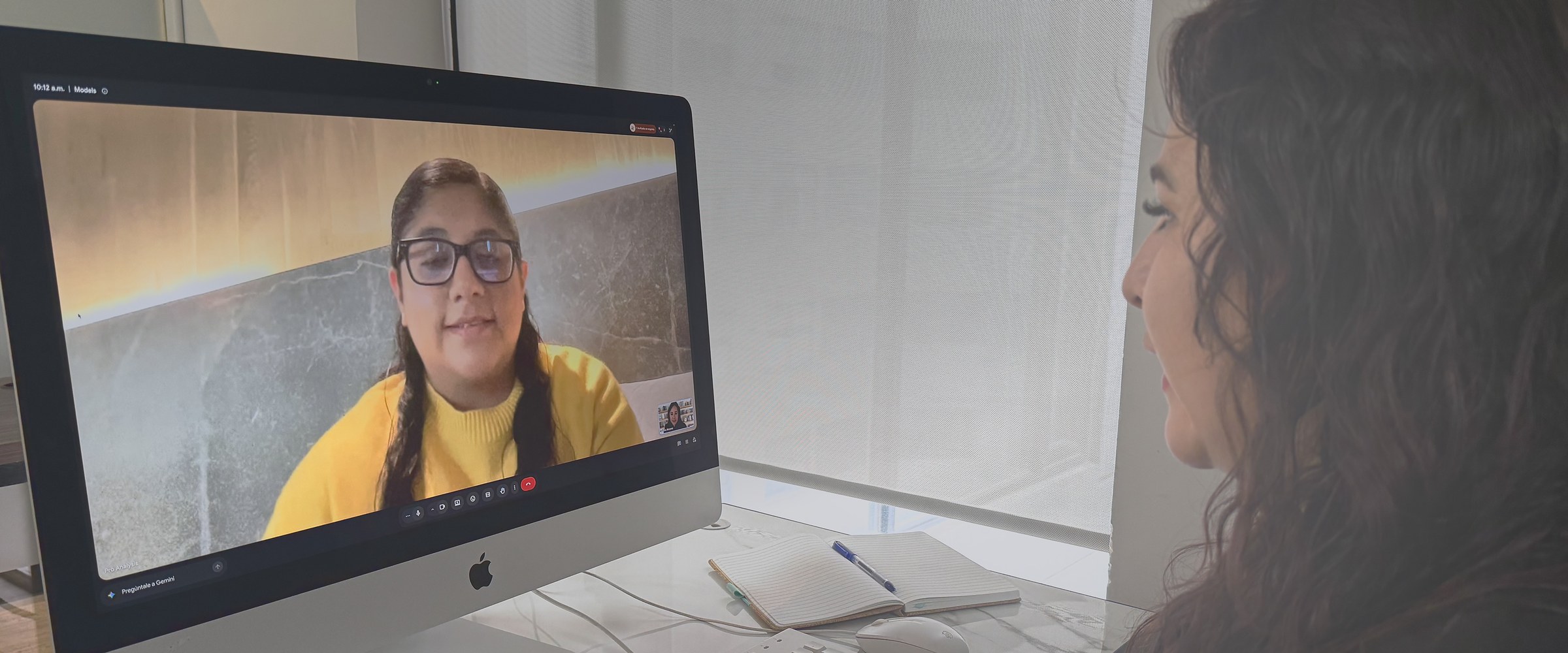 Una psicologa en su escritorio realizando una entrevista de evaluacion virtual, con la persona evaluada en la pantalla.